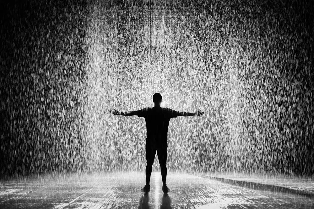 Silhueta de homem de braços abertos sob a chuva, símbolo de amor fati, aceitar o destino