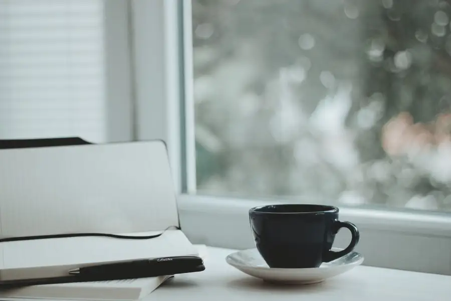 Xícara de café e caderno junto à janela, para anotar o que ainda é possível fazer