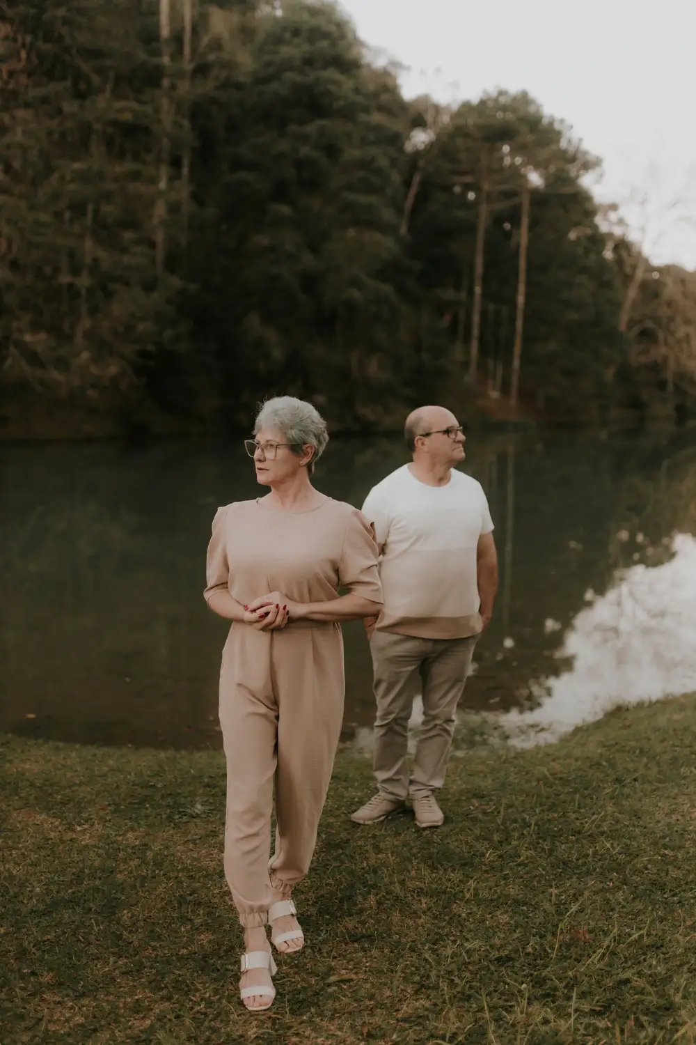Casal de idosos caminhando em silêncio à beira de um lago
