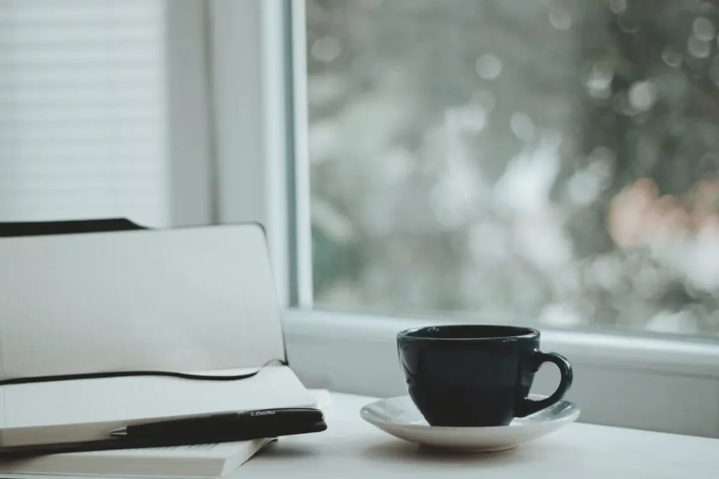 Caderno e xícara de café perto da janela, momento do diário estoico