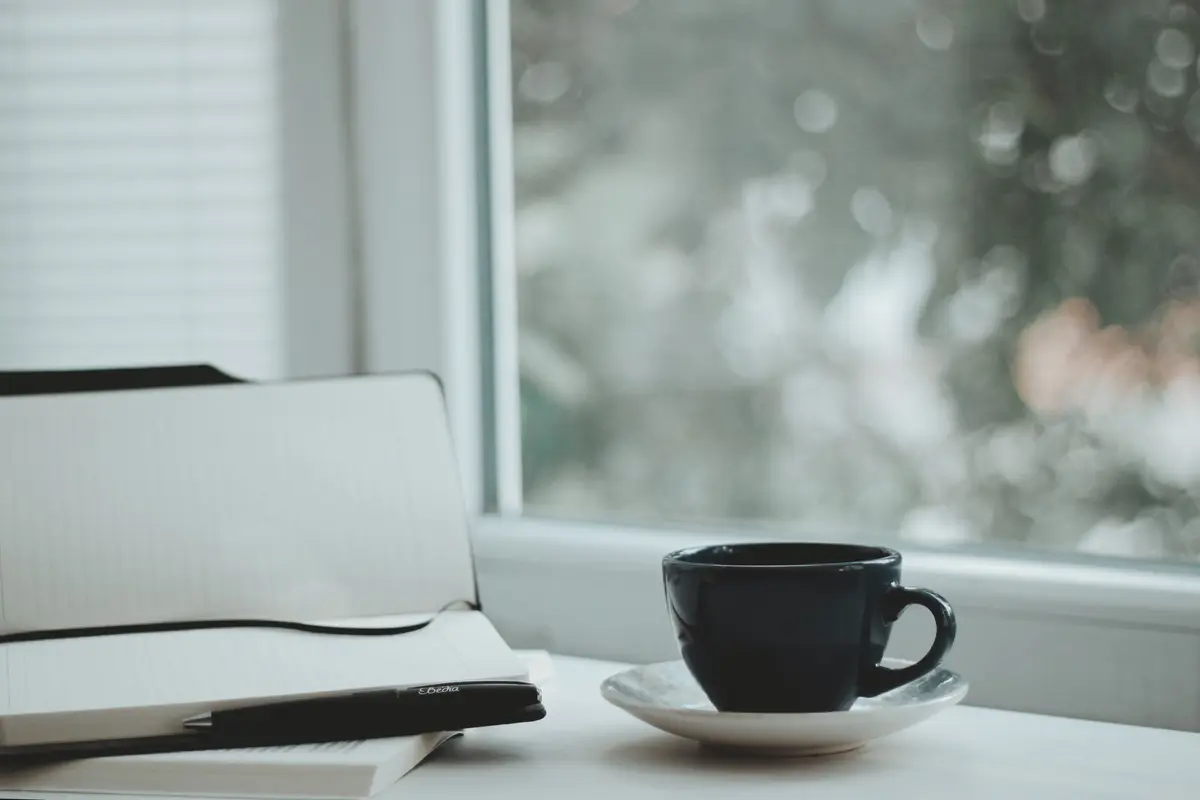 Caderno e xícara de café perto da janela, momento do diário estoico