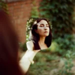 Mulher de olhos fechados refletida num espelho entre plantas, tema de estoicismo e autoestima