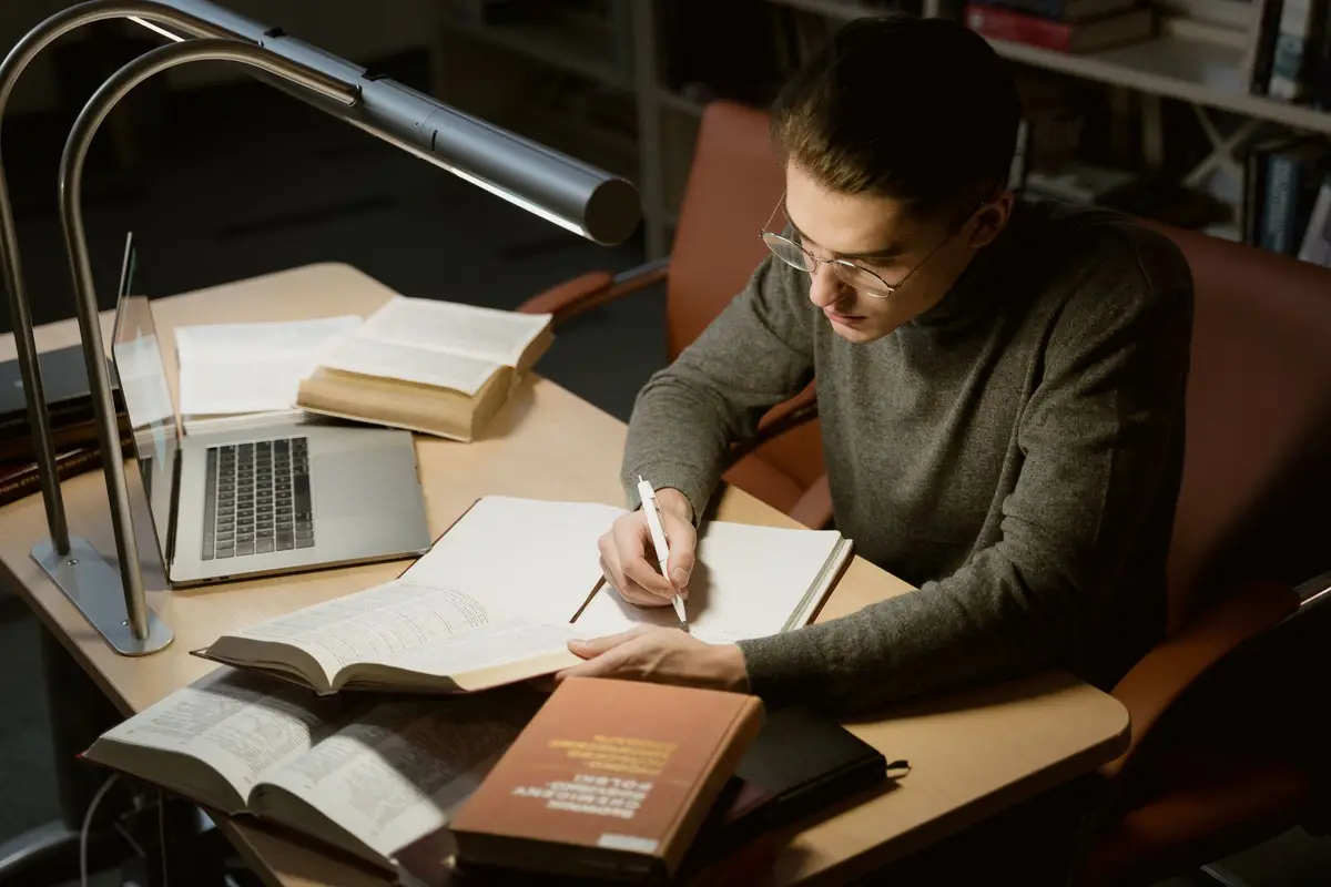 Estudante fazendo anotações sob a luminária, preparando-se para as provas