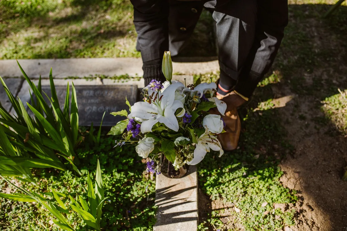 Pessoa deixando um vaso de flores brancas junto a um túmulo