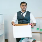 Homem saindo do escritório com seus objetos numa caixa de papelão