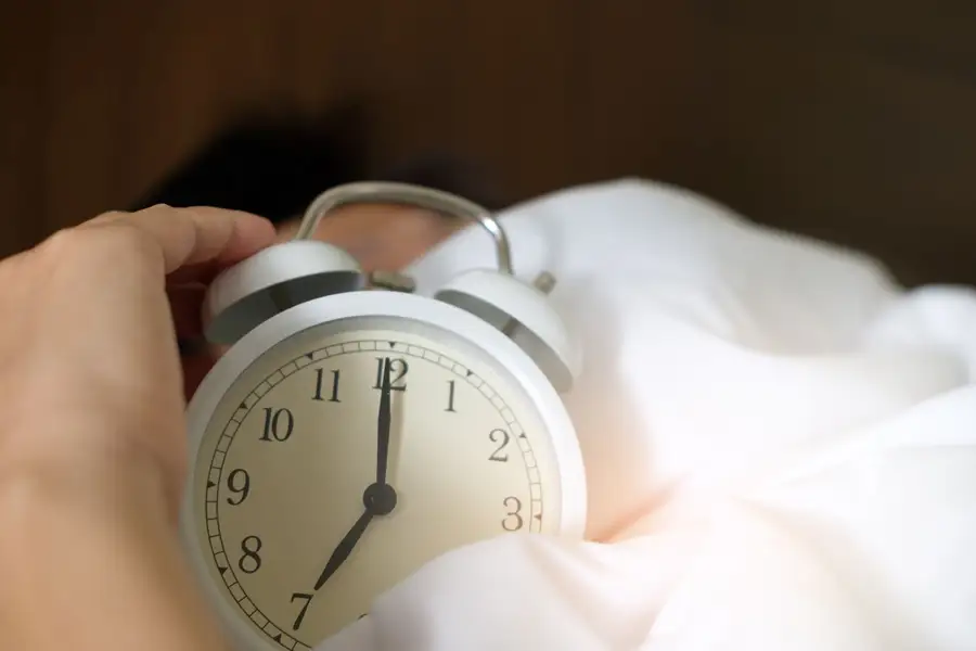Mão desligando o despertador na cama, a luta matinal que Marco Aurélio descreve