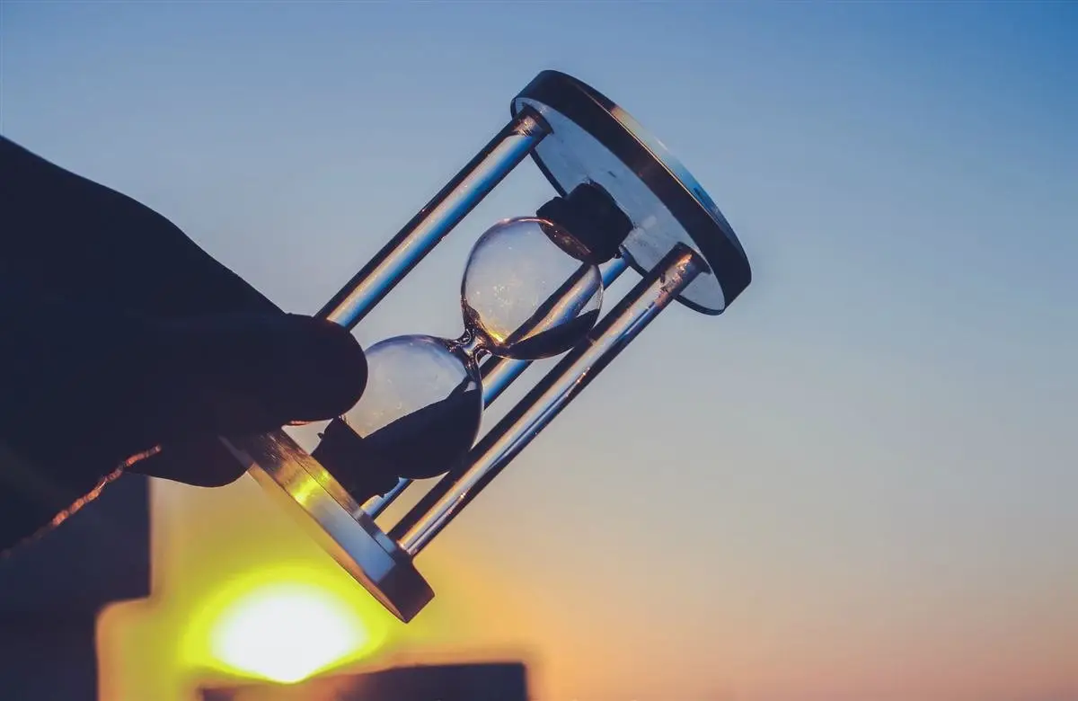 Mão segurando uma ampulheta contra o sol, lembrando que o tempo é limitado