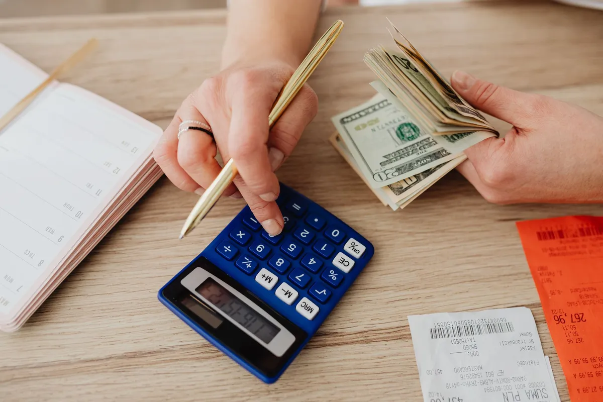 Mãos usando calculadora e contando dinheiro para organizar o orçamento