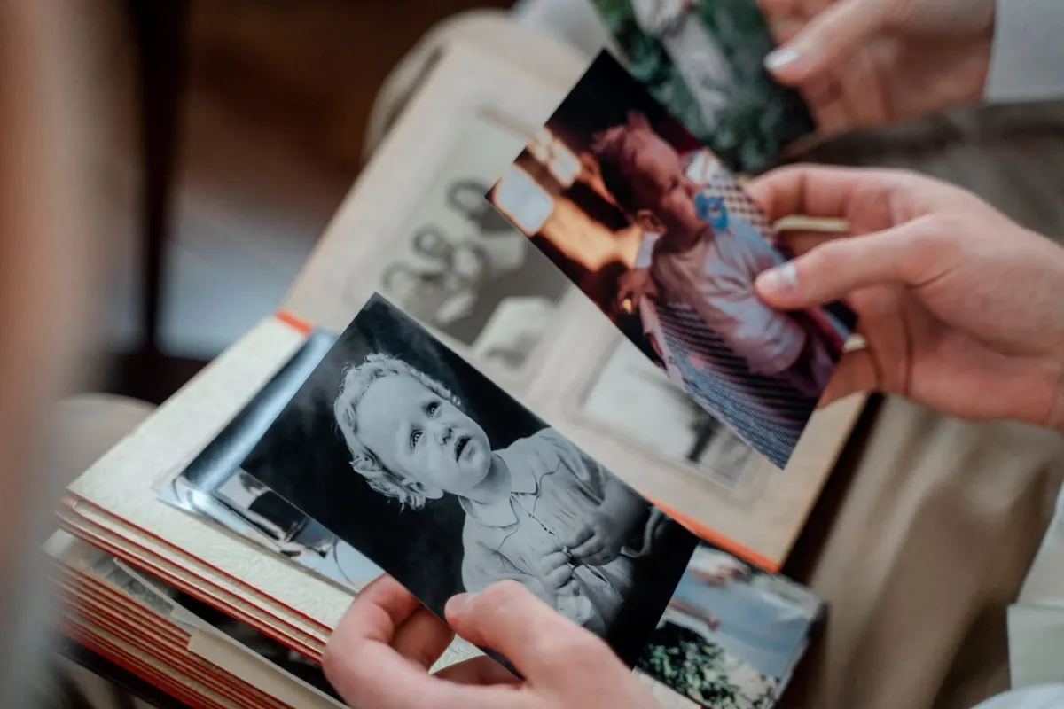 Mãos segurando fotos antigas de família de um álbum, lembrança de quem partiu