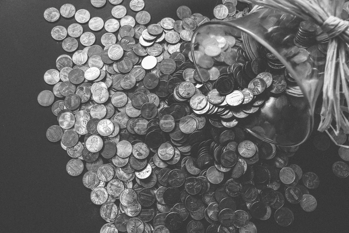 Moedas espalhadas saindo de um pote de vidro, em preto e branco