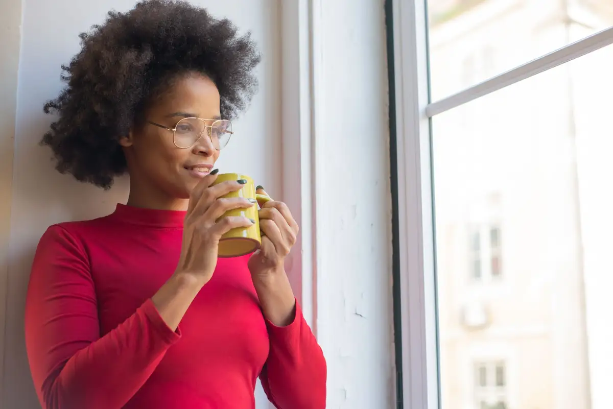 Mulher com café olhando pela janela, pensando em como aplicar o estoicismo no dia a dia