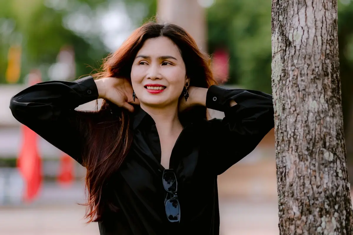 Mulher tranquila e sorridente encostada numa árvore no parque