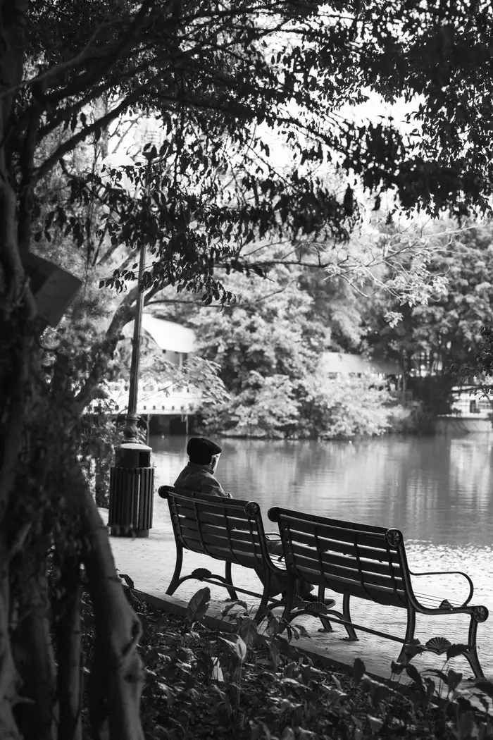 Pessoa sentada sozinha num banco junto ao lago, em preto e branco