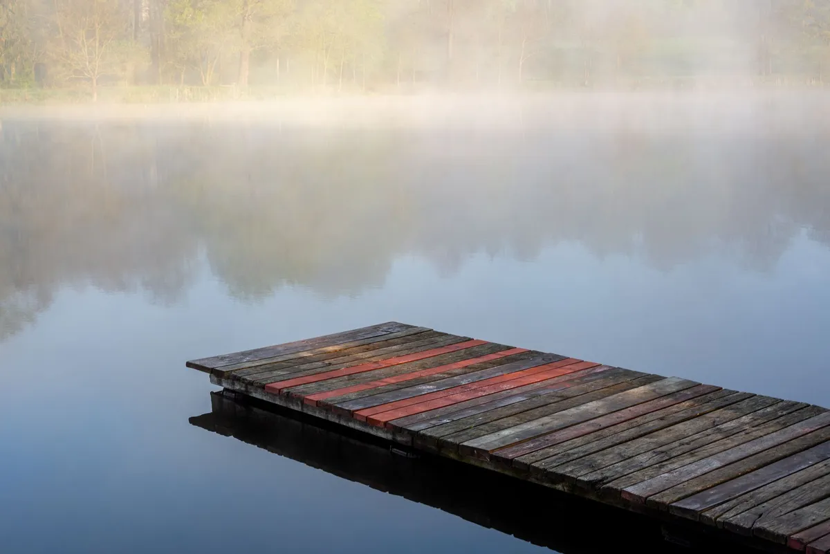Píer de madeira em lago sereno coberto de neblina