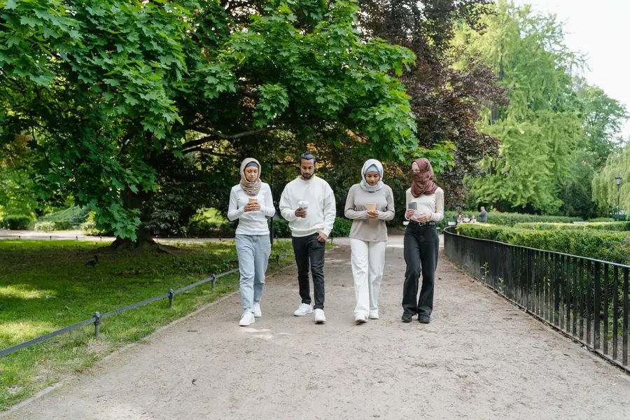 Amigos caminhando juntos num parque arborizado, vínculos que equilibram estoicismo e solidão