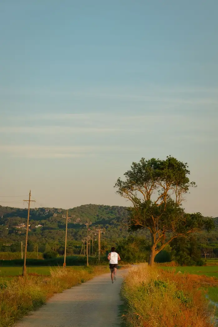 Corredor numa estrada de terra entre campos ao nascer do sol