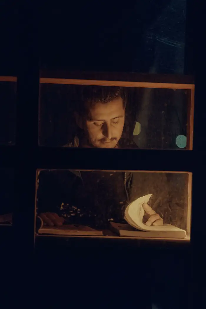 Homem lendo sozinho à noite, perto de uma janela iluminada