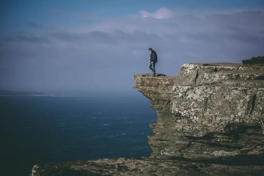 Homem de pé no alto de um penhasco sobre o mar, imagem de estoicismo e medo enfrentado com calma