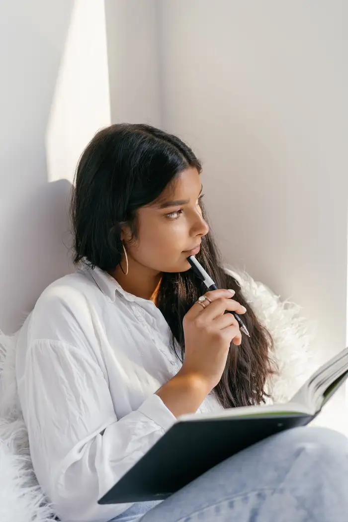 Jovem sentada junto à parede, refletindo com um caderno nas mãos
