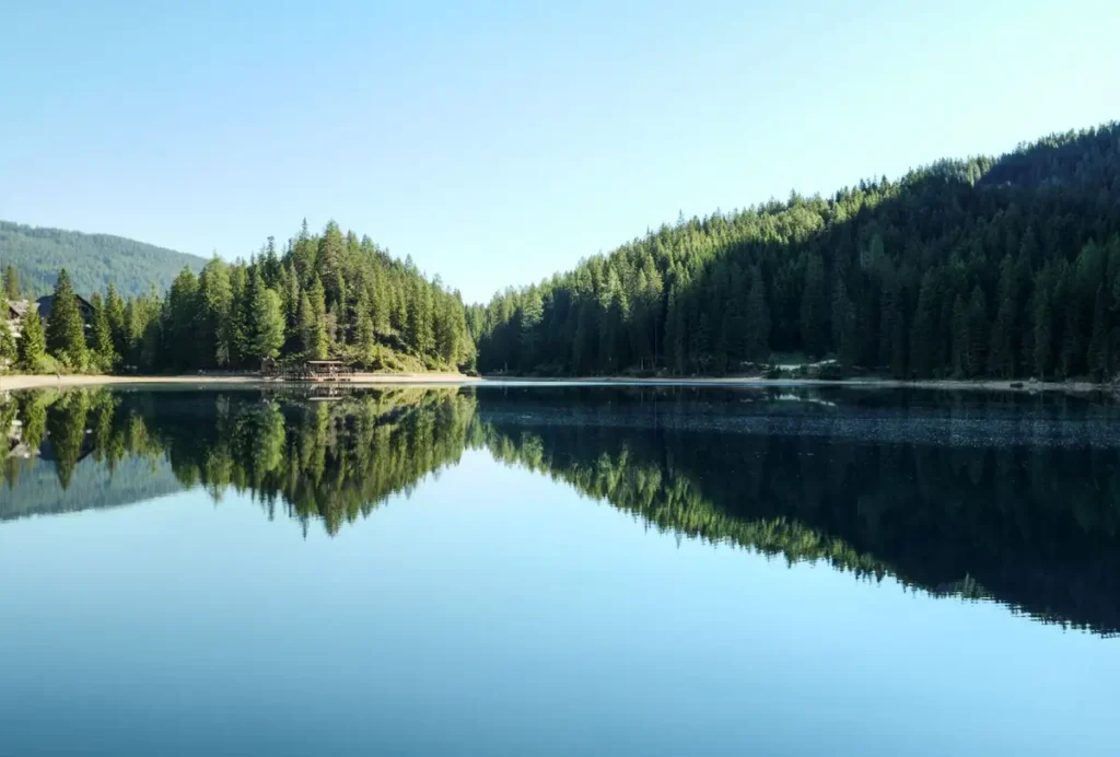 Lago calmo refletindo a floresta e o céu azul