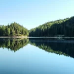 Lago calmo refletindo a floresta e o céu azul
