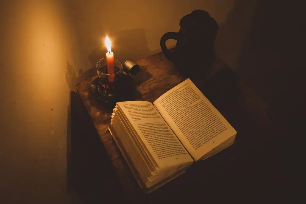 Livro antigo aberto sobre a mesa, iluminado pela luz de uma vela