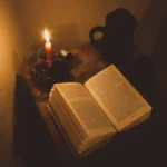 Livro antigo aberto sobre a mesa, iluminado pela luz de uma vela