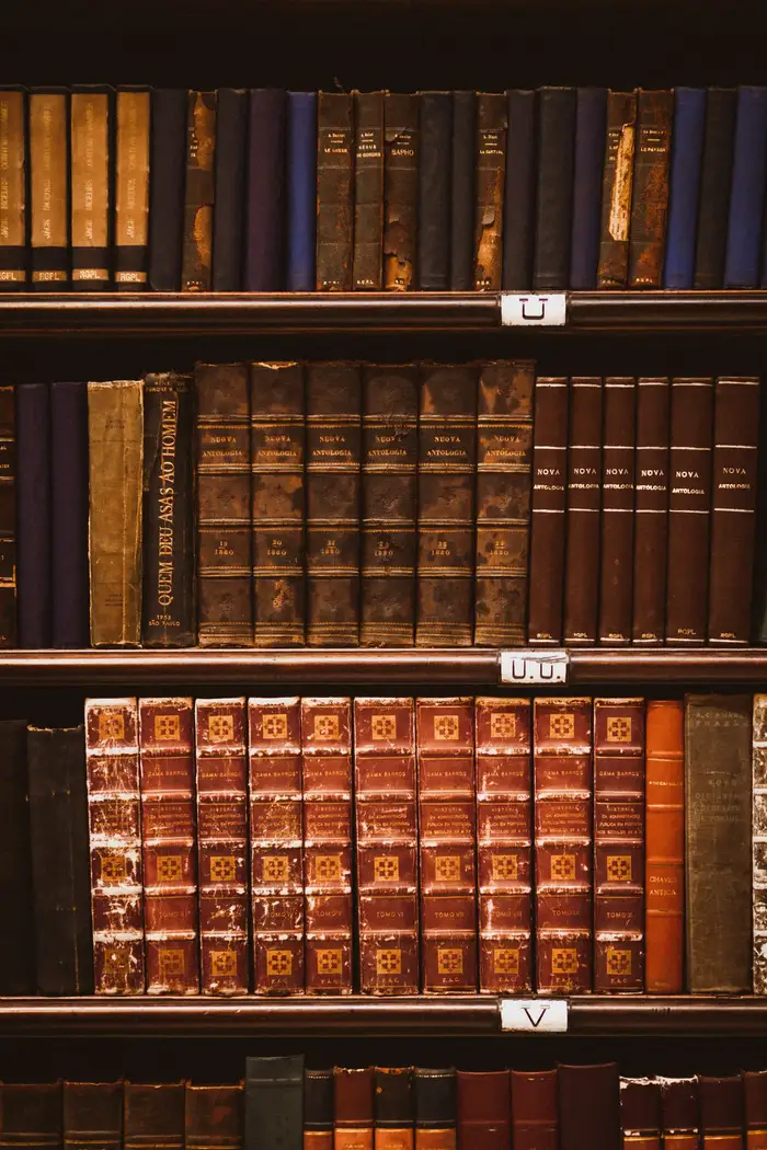 Livros antigos encadernados em couro numa estante de biblioteca