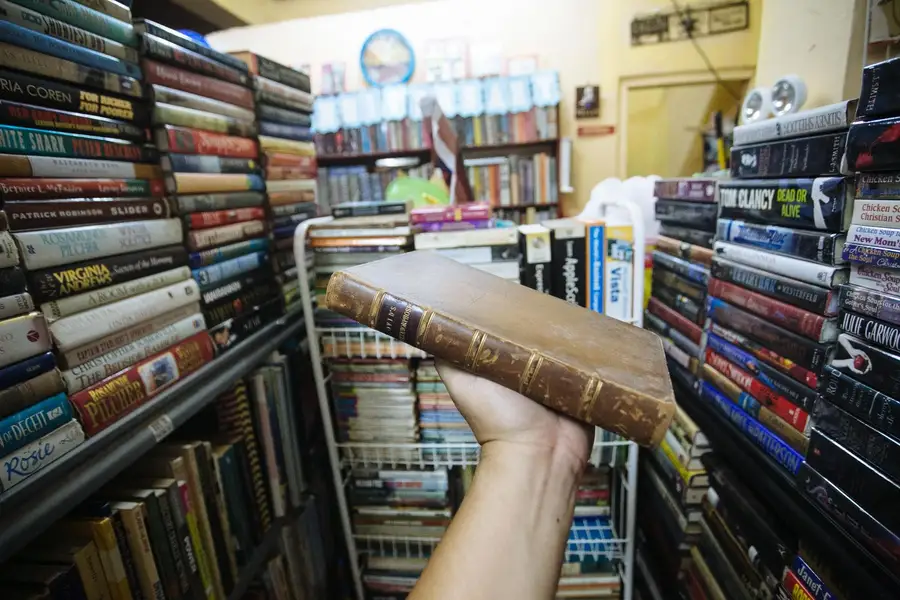 Mão segurando um livro antigo entre estantes cheias de livros