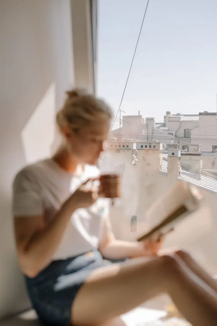 Mulher tomando café com um livro junto à janela