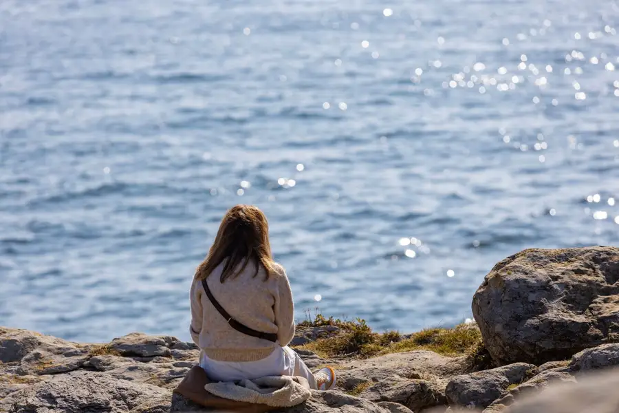 Mulher sentada nas pedras olhando o mar com calma