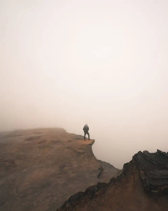 Pessoa sozinha na beira de um penhasco envolto em neblina